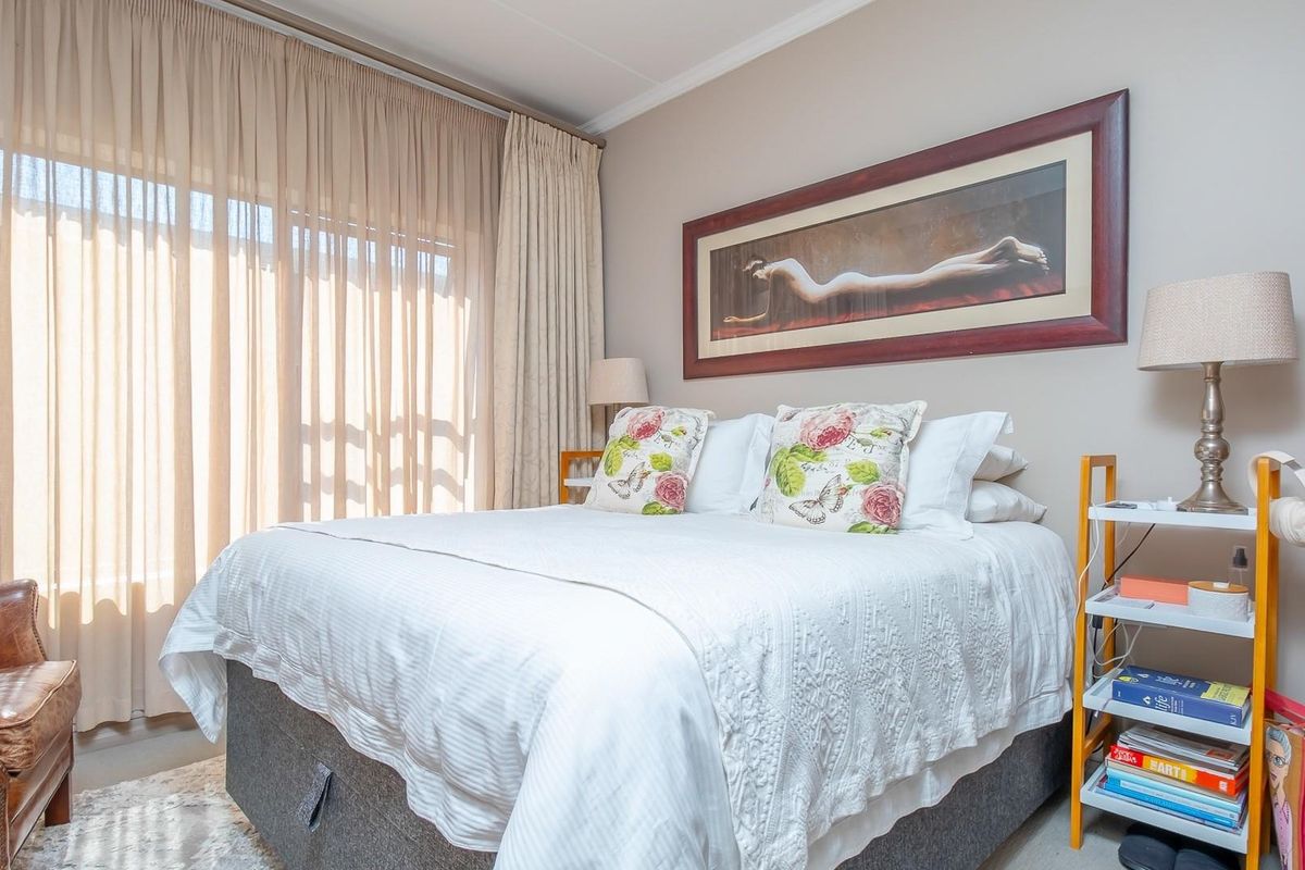 A well-lit bedroom featuring neutral wall tones, carpeted flooring, and a large sliding glass door with floor-to-ceiling curtains providing natural light.