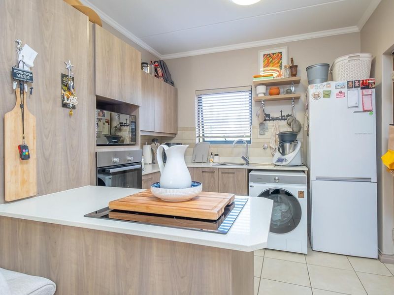 A functional kitchen featuring light wood-look cabinetry, stone countertops, integrated oven, hob, and dedicated space for laundry appliances.