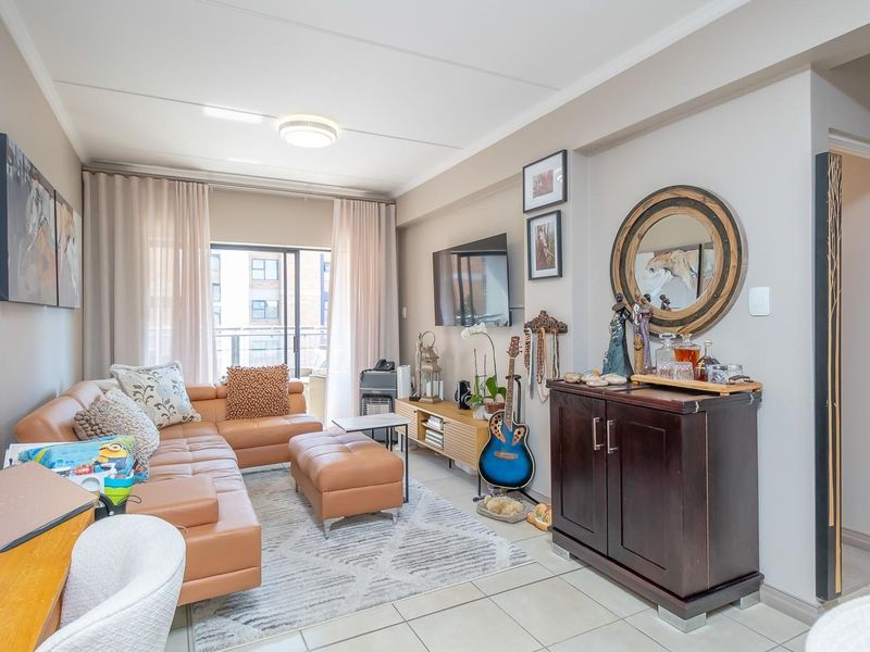 A well-maintained living room featuring tiled flooring and a sliding glass door providing access to the balcony.