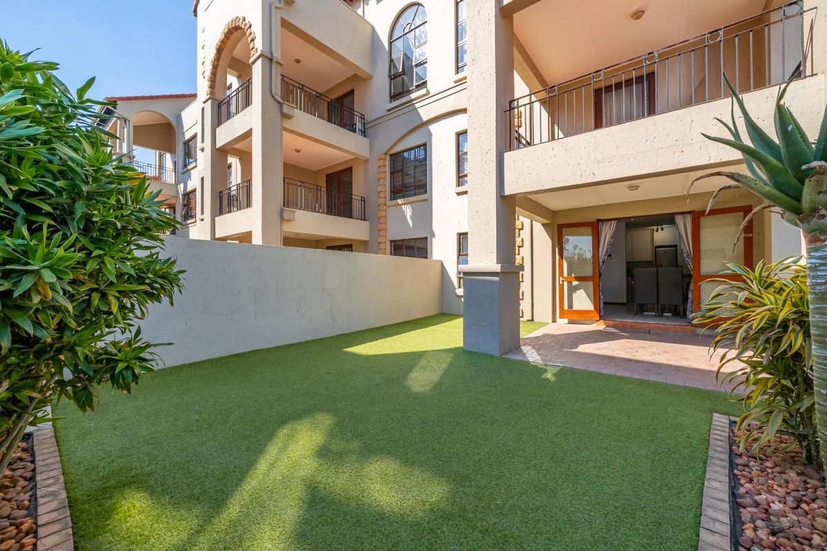 A well-maintained rear garden area featuring artificial turf, a paved patio, and access to the apartment's ground floor living space and upper-level balconies.