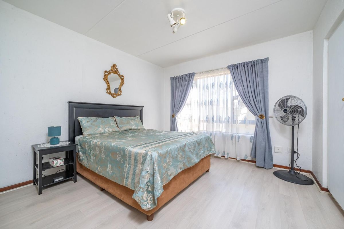 A well-lit bedroom featuring light-toned laminate flooring, neutral walls, and a large window dressed with curtains.