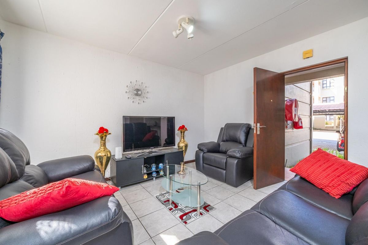 A compact living room featuring neutral tiled flooring and a ceiling-mounted spotlight fixture, providing direct access to the exterior walkway.