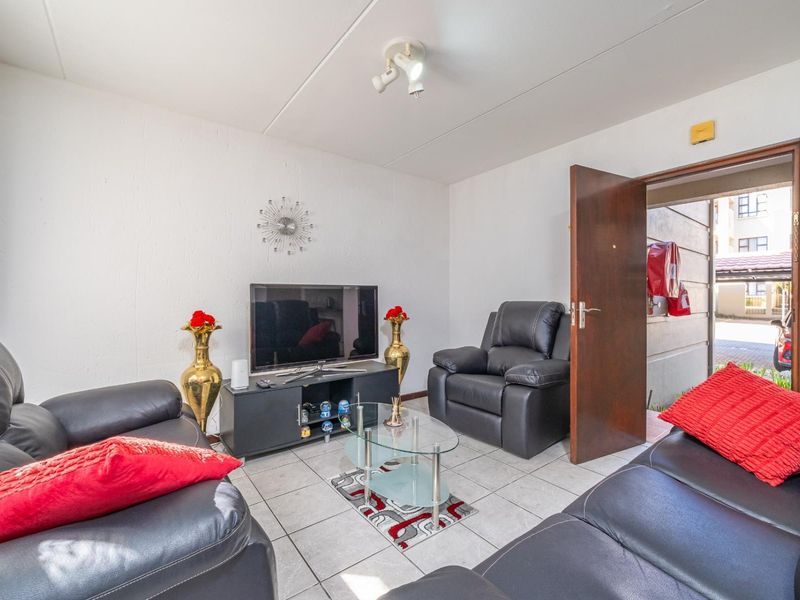 A compact living room featuring neutral tiled flooring and a ceiling-mounted spotlight fixture, providing direct access to the exterior walkway.