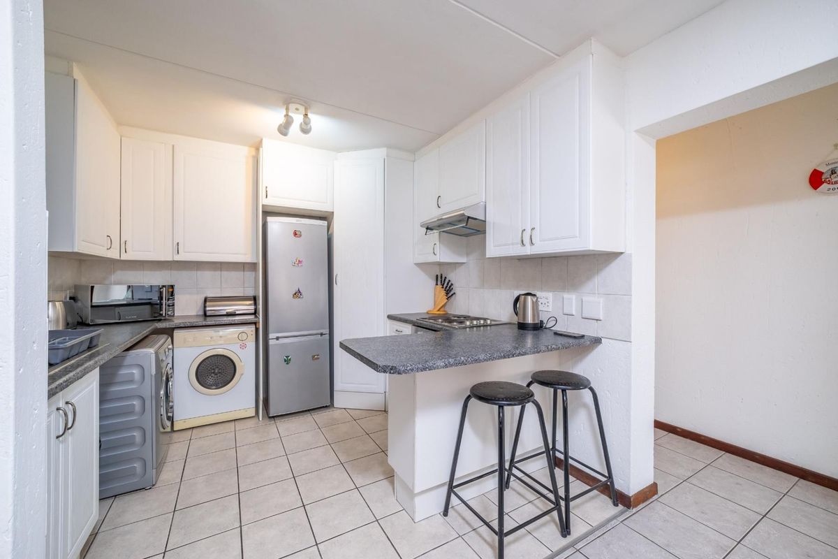 A functional kitchen featuring white cabinetry, dark laminate countertops, a breakfast bar, and tiled flooring, providing a practical layout for daily meal preparation.