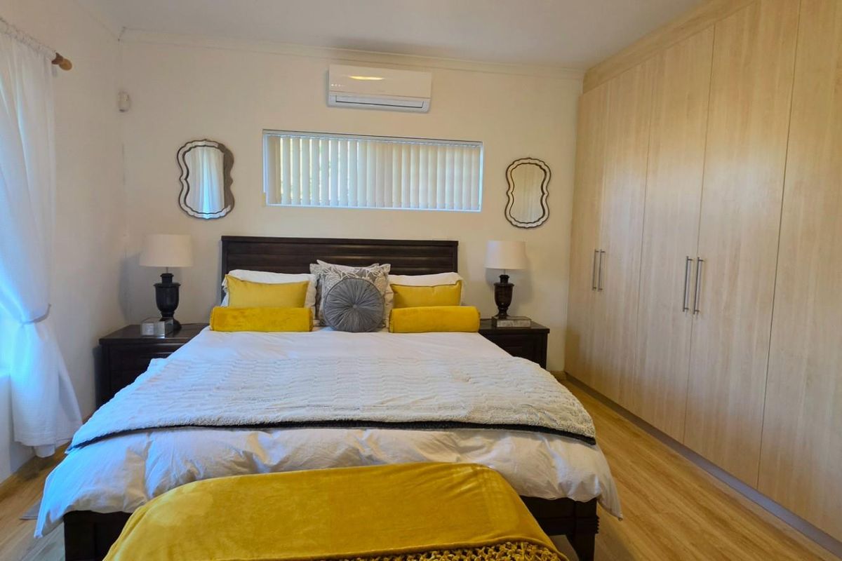 A well-maintained bedroom featuring light wood-finish built-in cupboards, laminate flooring, and a wall-mounted air conditioning unit.