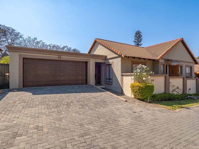 Front elevation of a well-maintained house featuring a paved driveway, double garage, and secure boundary walling.