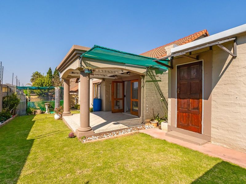 Rear view of the property featuring a covered patio with concrete columns, a small lawn, and secure boundary walls with electric fencing.