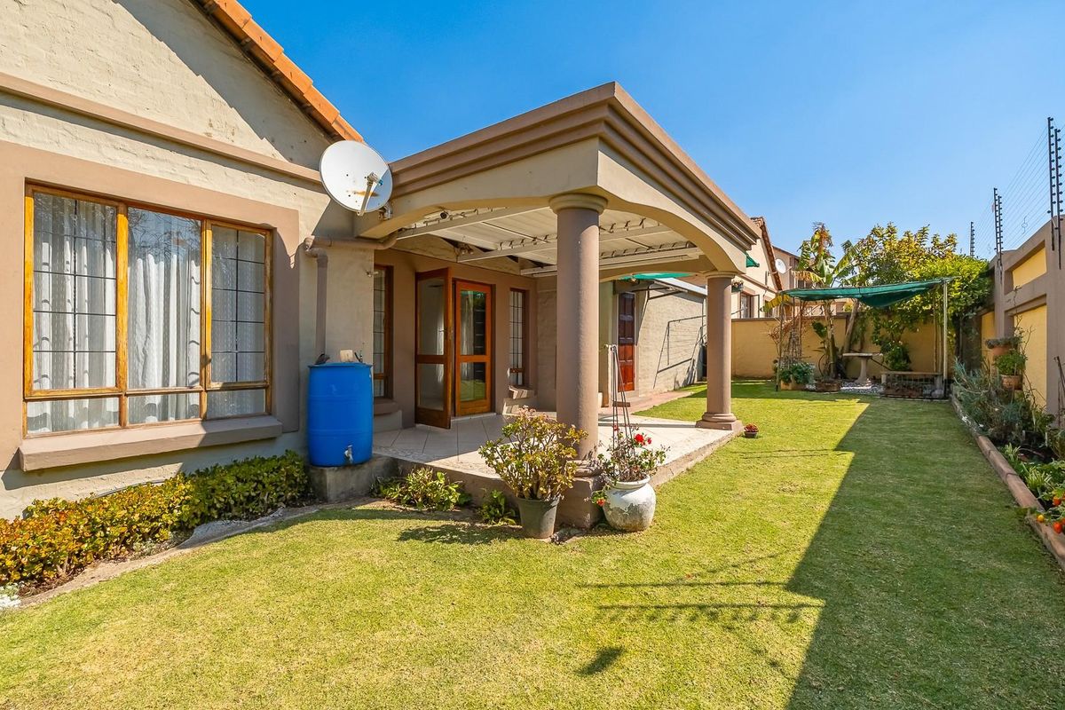 Rear view of the property featuring a covered patio with concrete columns, a well-maintained lawn, and secure boundary walls with electric fencing.