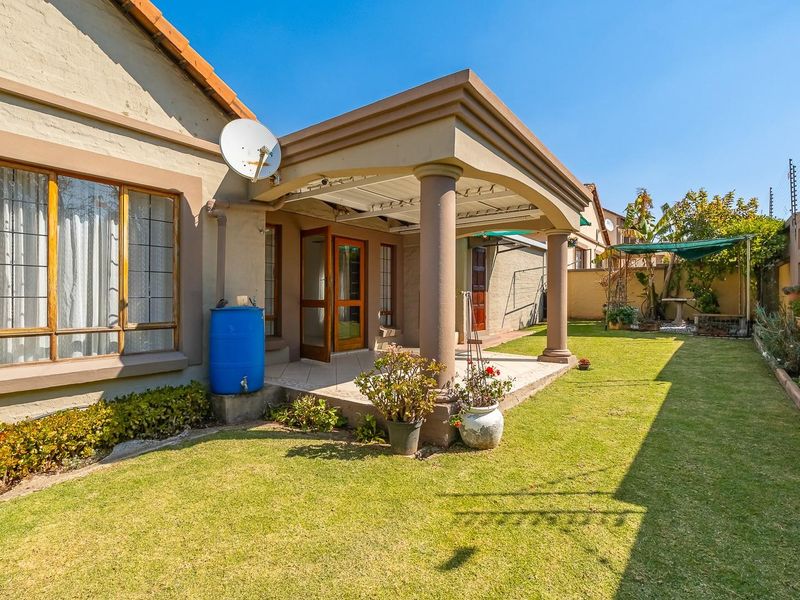 Rear view of the property featuring a covered patio with concrete columns, a well-maintained lawn, and secure boundary walls with electric fencing.