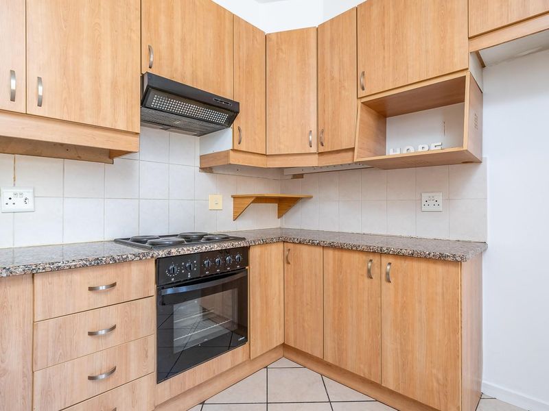 A functional kitchen featuring light wood-finish cabinetry, granite countertops, a built-in oven with hob, and a tiled backsplash.