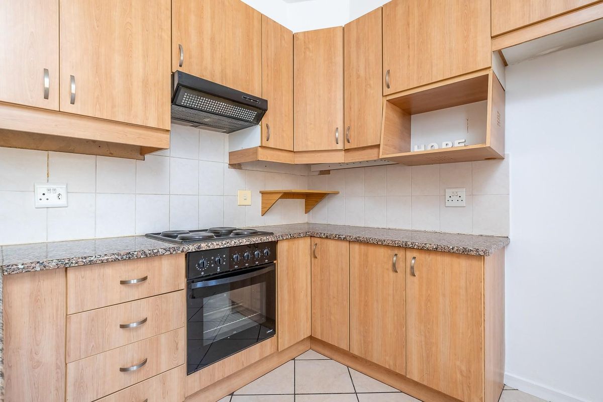 A functional kitchen featuring light wood-finish cabinetry, granite countertops, a built-in oven with hob, and a tiled backsplash.