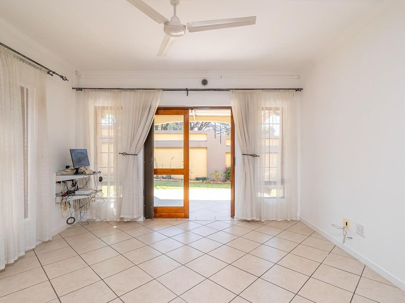 Bright and spacious living area featuring neutral tiled flooring, a ceiling fan, and direct access to the outdoor patio through sliding glass doors.