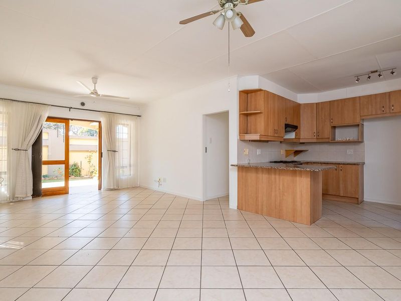 Spacious open-plan living area featuring tiled floors, a ceiling fan, and a functional kitchen with granite countertops and wooden cabinetry, leading to an outdoor patio.