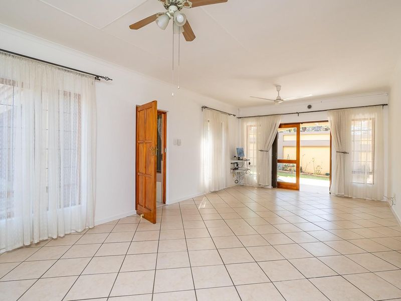 Spacious open-plan living area featuring neutral tiled flooring, ceiling fans, and direct access to the rear garden through sliding glass doors.