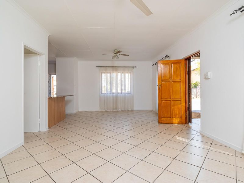 Spacious open-plan living area featuring neutral tiled flooring, ceiling fans, and direct access to the exterior through a solid timber door.