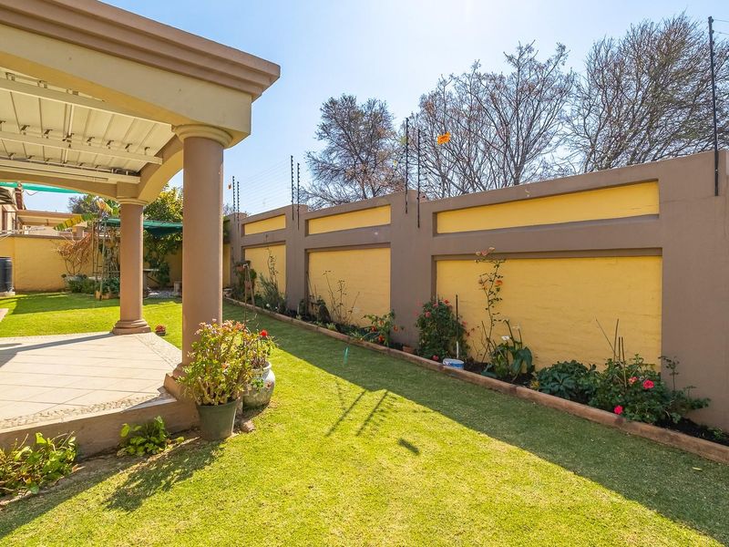 A well-maintained rear garden featuring a covered patio with tiled flooring, concrete columns, and a secure perimeter wall with electric fencing.
