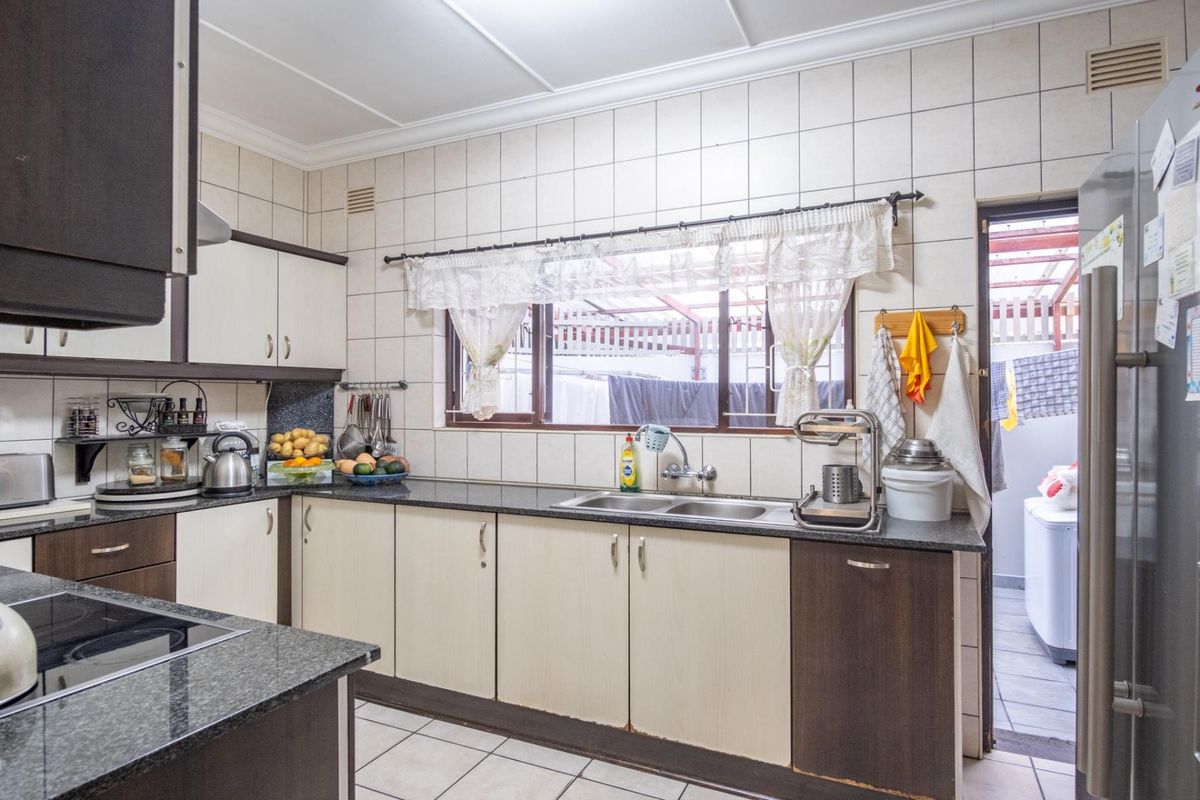 A functional kitchen featuring granite countertops, double basin sink, and built-in cabinetry with tiled walls and floors, offering a practical layout for daily use.