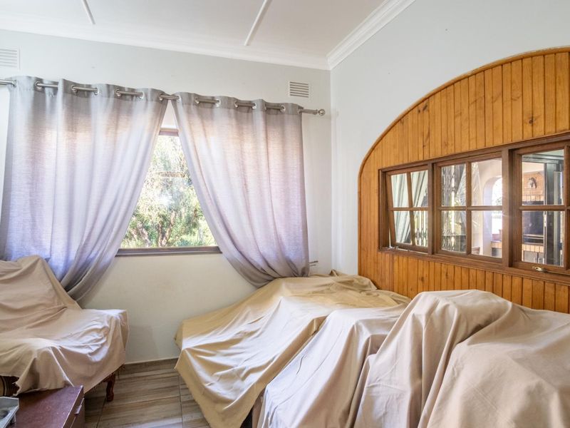 A bedroom featuring timber wall paneling, an internal window looking into an adjacent space, and tiled flooring.