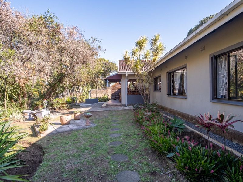 A view of the rear garden featuring a paved patio area, landscaped garden beds, and a stepped pathway alongside the house exterior.