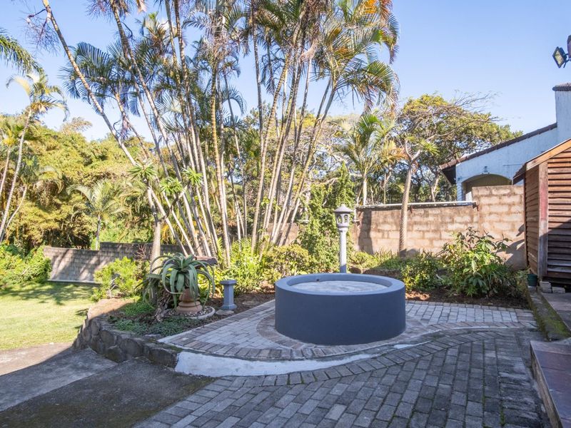 A landscaped garden area featuring brick paving, a central concrete water feature, and mature palm trees set against a perimeter wall.