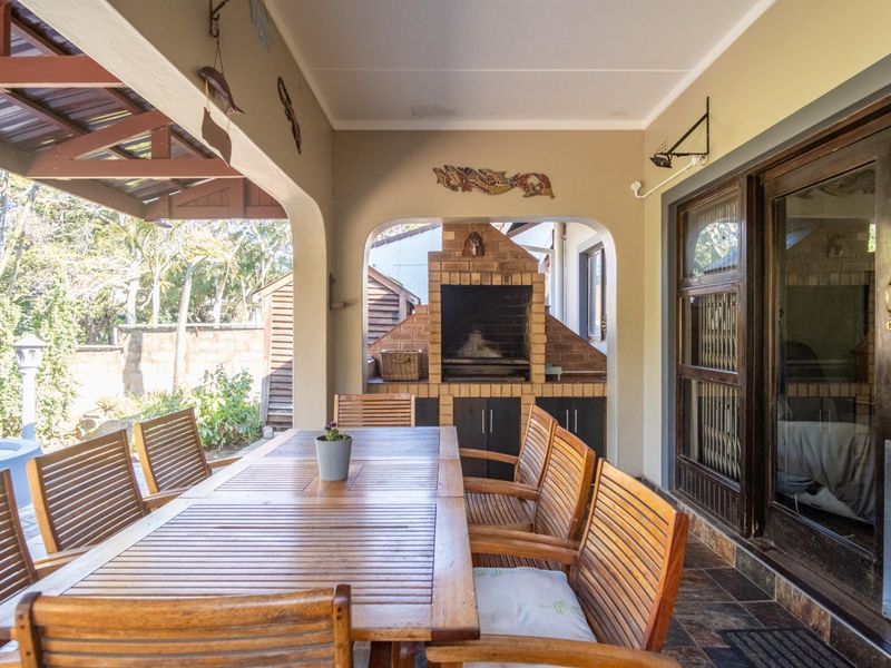 Covered patio area featuring a built-in brick braai, tiled flooring, and timber-framed sliding doors leading into the home.