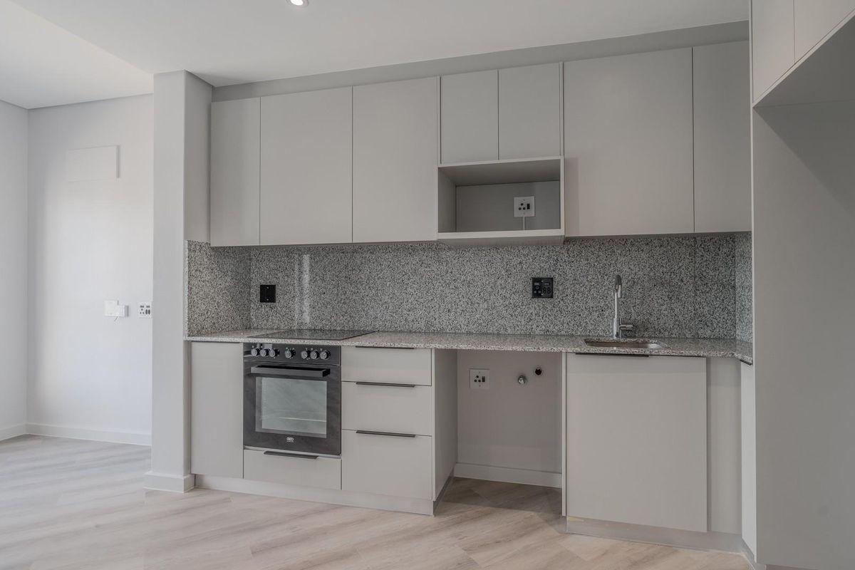 Modern kitchen featuring light grey cabinetry, granite countertops, integrated oven and hob, and space for an under-counter appliance.