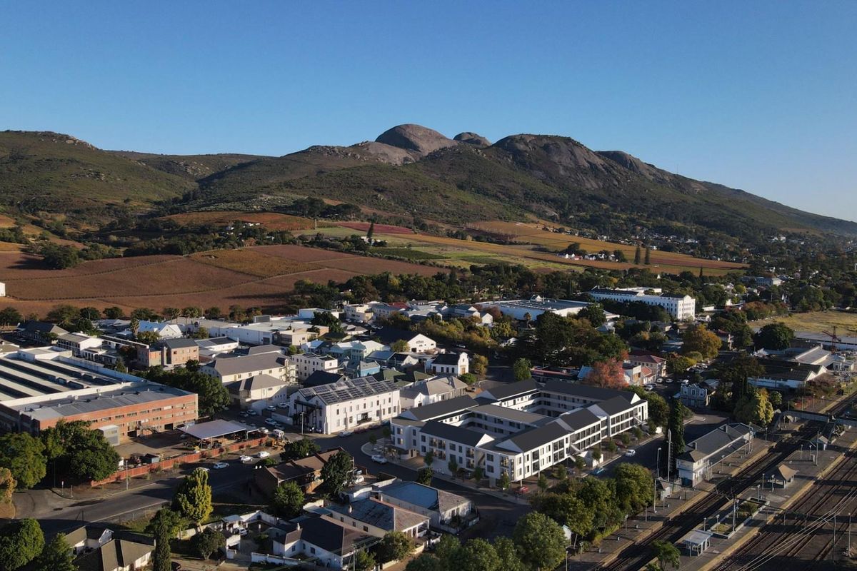 Aerial view of the apartment complex situated in a scenic town setting with mountain views and proximity to local transport infrastructure.