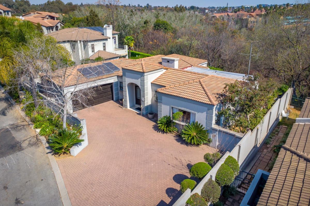 Aerial view of a residential property featuring a tiled roof, solar panels, a spacious paved driveway, and a double garage within a secure estate.