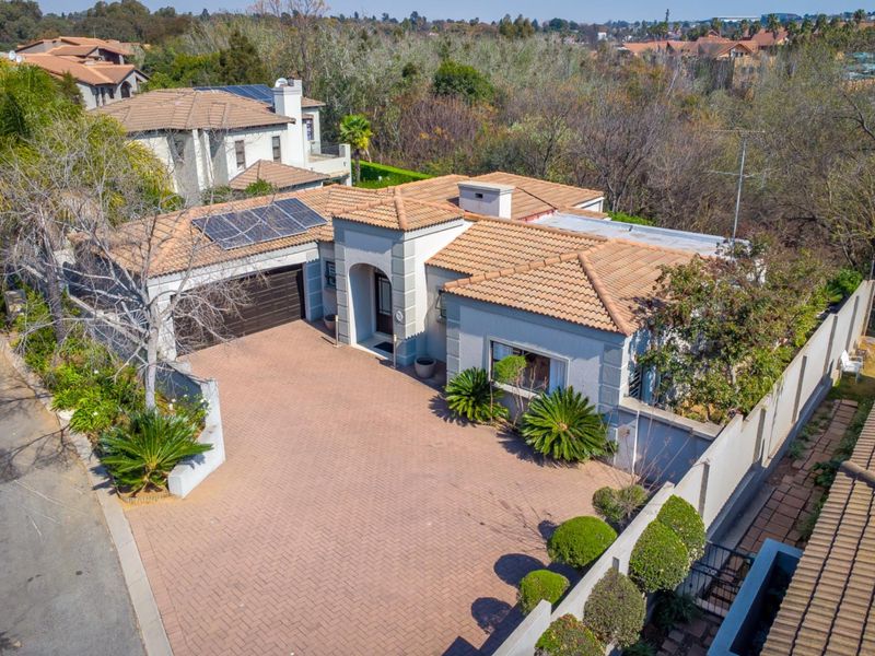 Aerial view of a residential property featuring a tiled roof, solar panels, a spacious paved driveway, and a double garage within a secure estate.