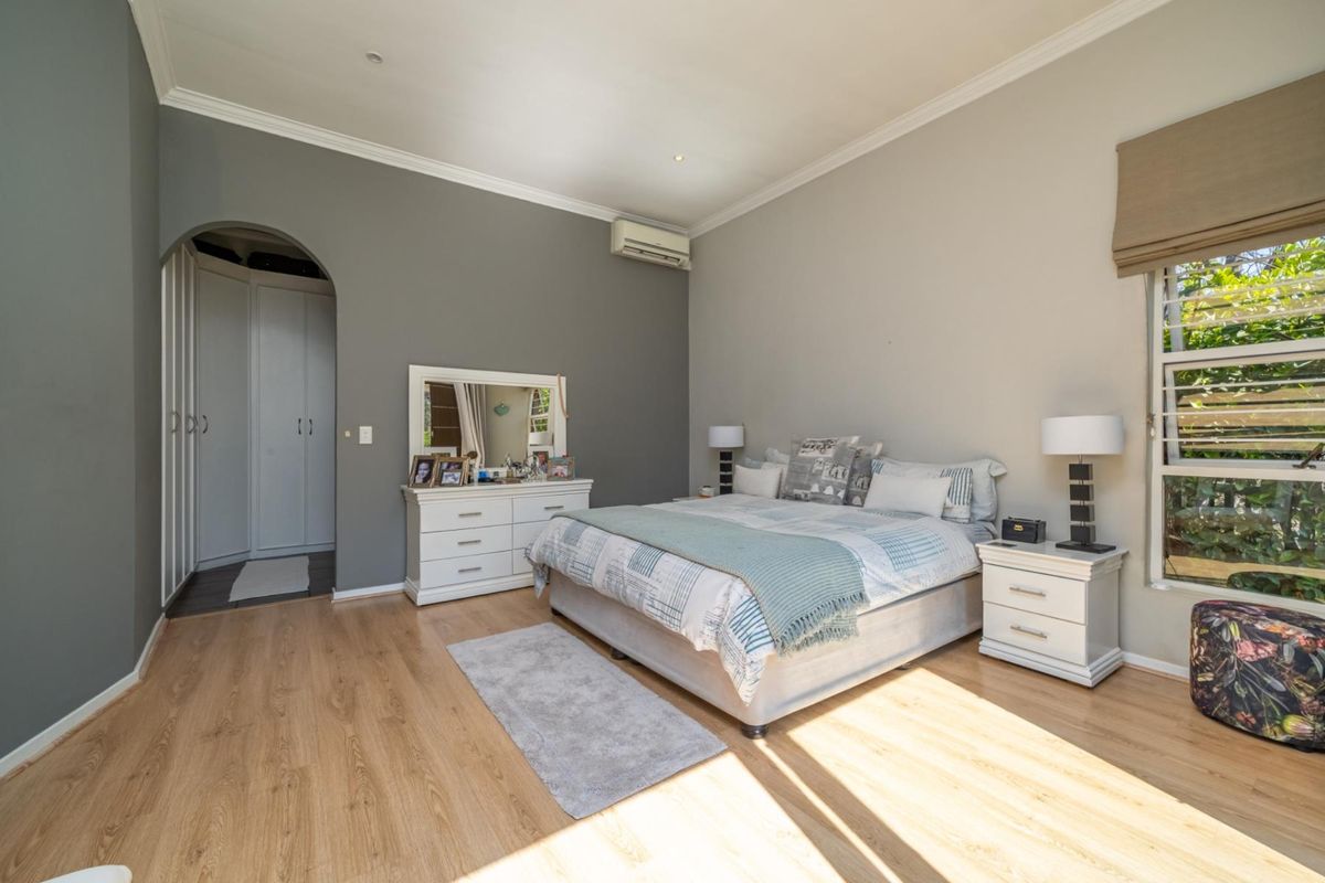 Spacious bedroom featuring laminate flooring, built-in cupboards with an arched entry, and a wall-mounted air conditioning unit.