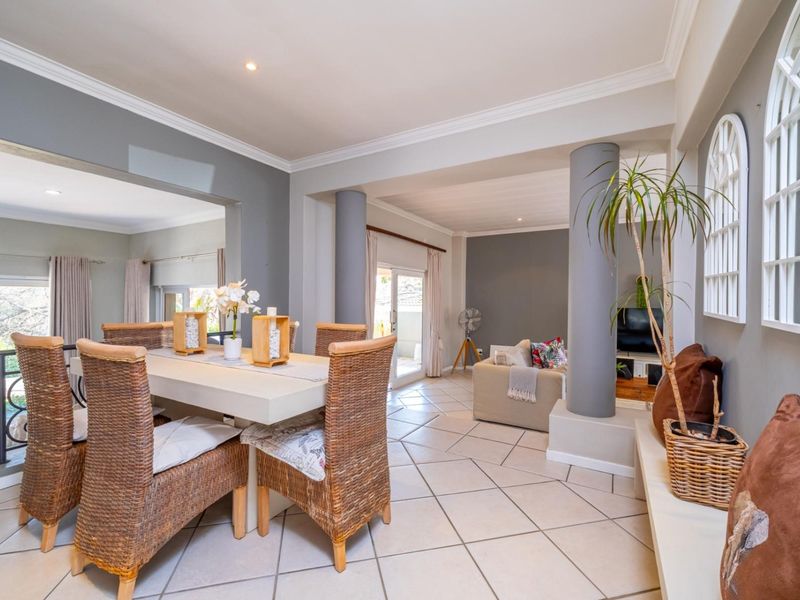 Spacious open-plan living and dining area featuring neutral grey walls, ceramic tiled flooring, structural columns, and abundant natural light through sliding glass doors.