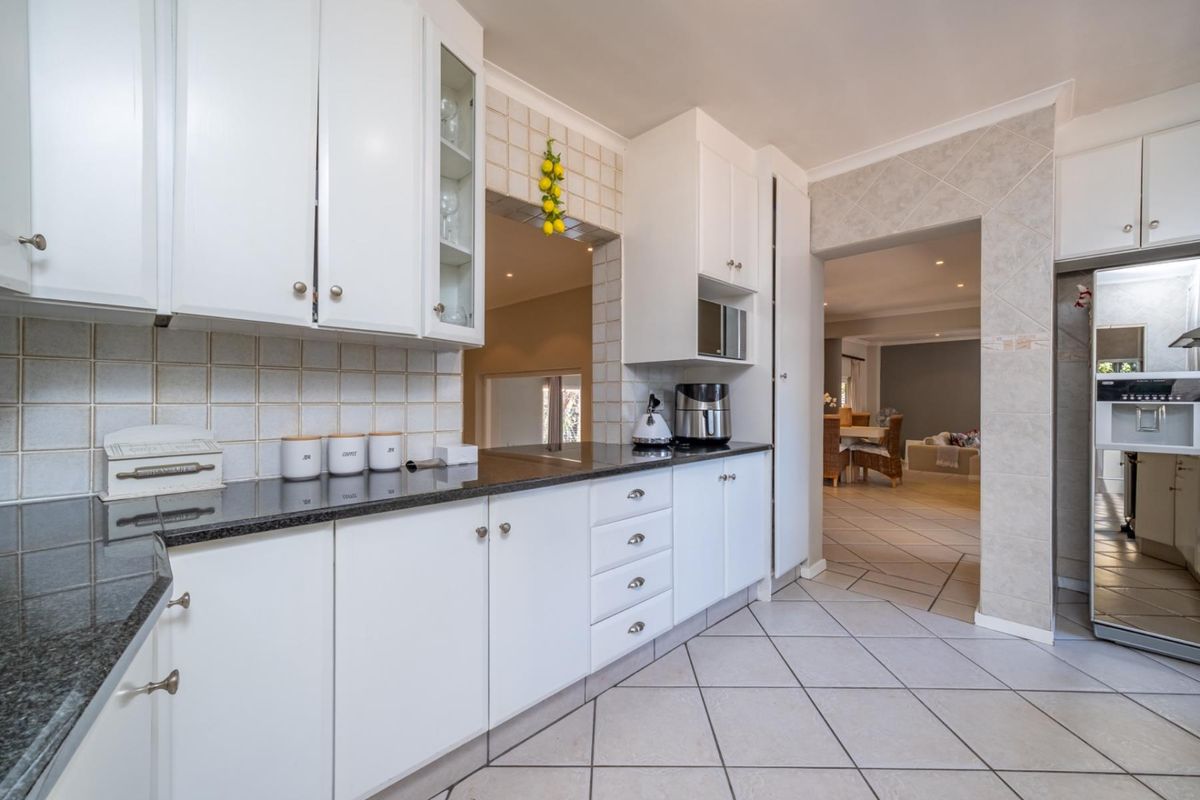 A well-maintained kitchen featuring white cabinetry, granite countertops, tiled backsplash, and tiled flooring, with an open flow into the adjacent living area.