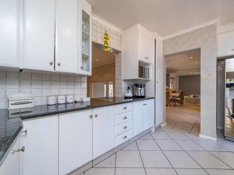 A well-maintained kitchen featuring white cabinetry, granite countertops, tiled backsplash, and tiled flooring, with an open flow into the adjacent living area.