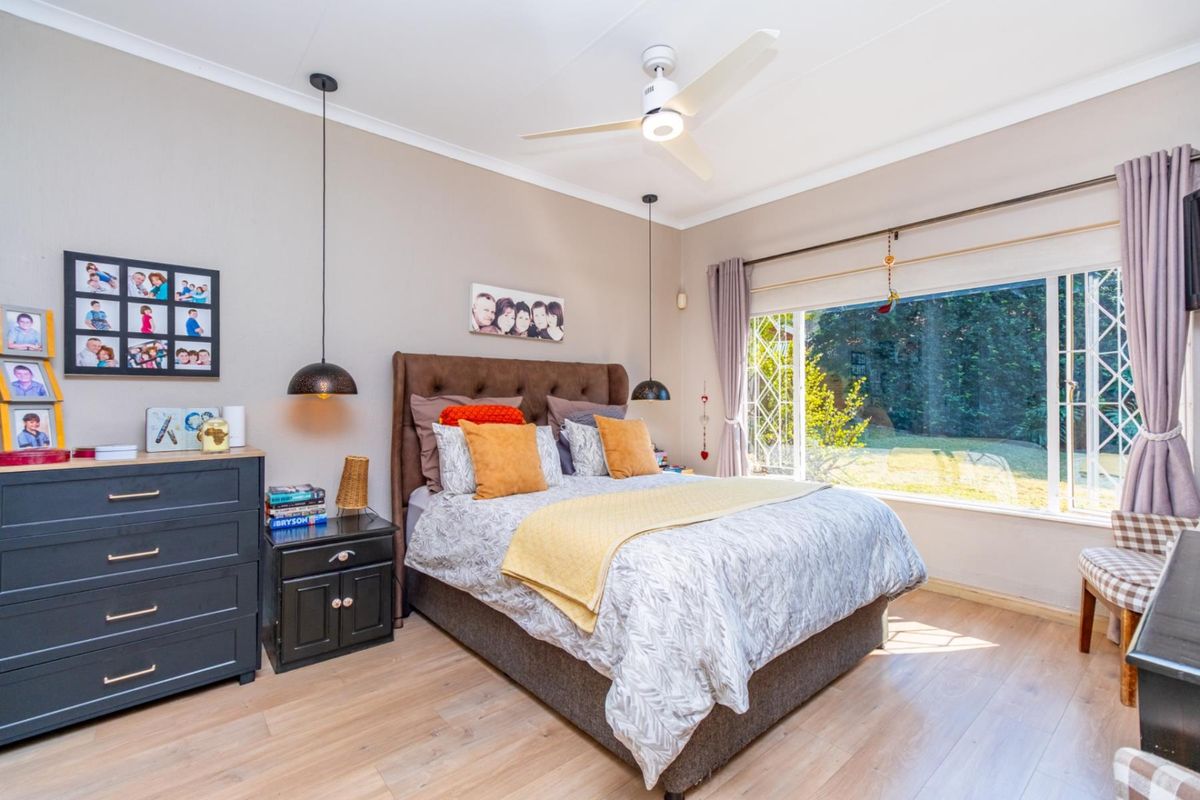A well-maintained bedroom featuring laminate flooring, a ceiling fan, and large windows with security gates overlooking the garden.