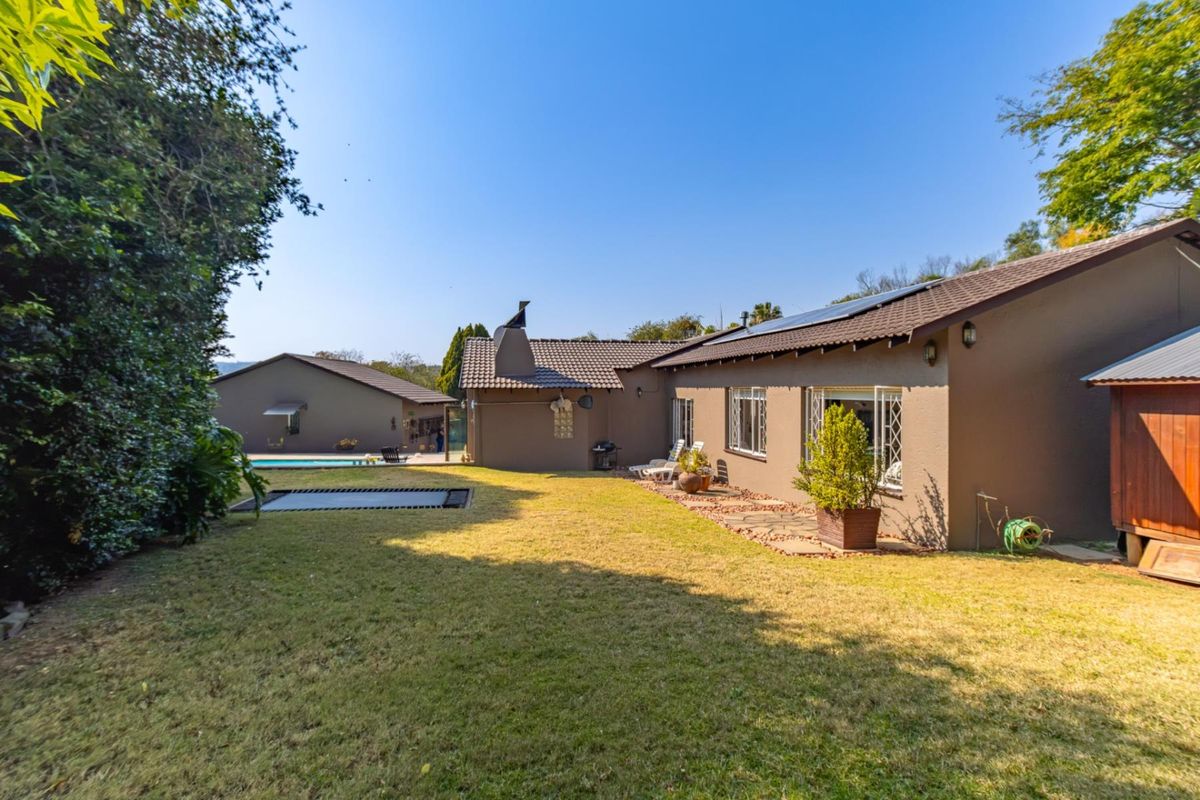 Rear view of the house featuring a spacious lawn, paved patio area, swimming pool, and solar panels installed on the tiled roof.
