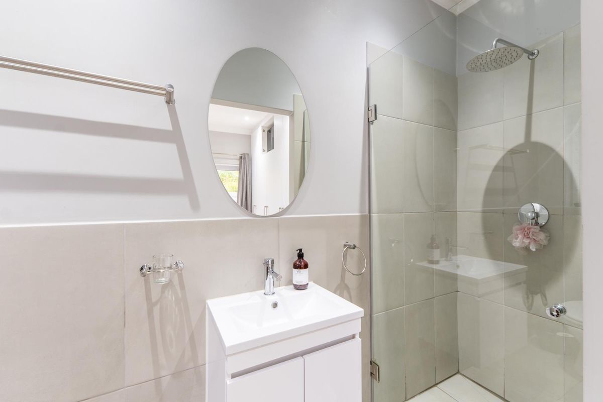 Modern bathroom featuring a sleek vanity, oval mirror, and a spacious walk-in shower with a rain shower head and glass enclosure.