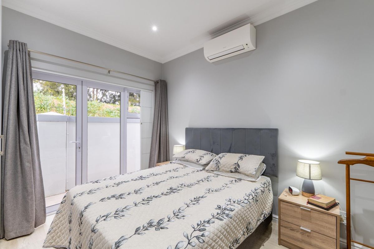 A well-maintained bedroom featuring neutral walls, recessed lighting, a wall-mounted air conditioning unit, and direct access to an outdoor area via sliding glass doors.