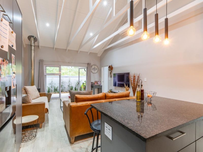 Modern open-plan living area featuring a vaulted ceiling with exposed rafters, a granite kitchen island, and a wood-burning fireplace leading to a private patio.