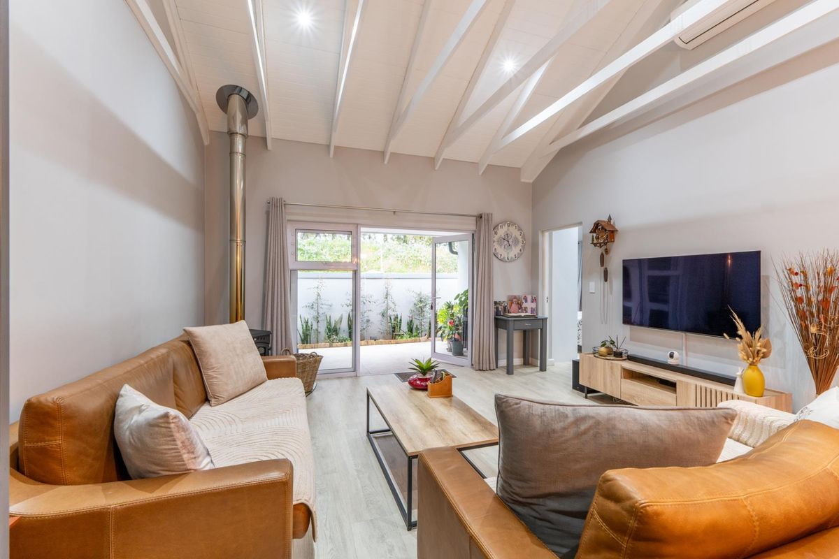 Bright living room featuring a vaulted ceiling with exposed rafters, a wood-burning fireplace, and sliding glass doors leading to an outdoor patio area.