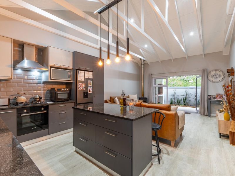 Modern open-plan kitchen and living area featuring a central island, granite countertops, exposed white trusses, and seamless flow to the outdoor patio.