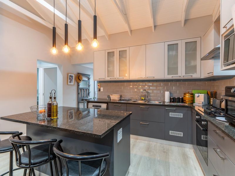 Modern kitchen featuring granite countertops, a central island, subway tile backsplash, and exposed beam ceilings with contemporary pendant lighting.
