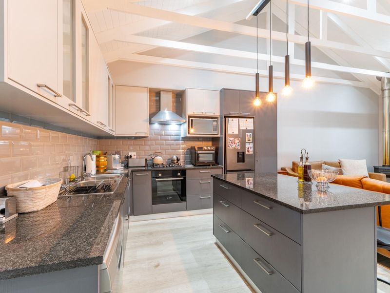 Modern open-plan kitchen featuring granite countertops, subway tile backsplash, and exposed timber rafters, seamlessly flowing into the living area with a wood-burning stove.
