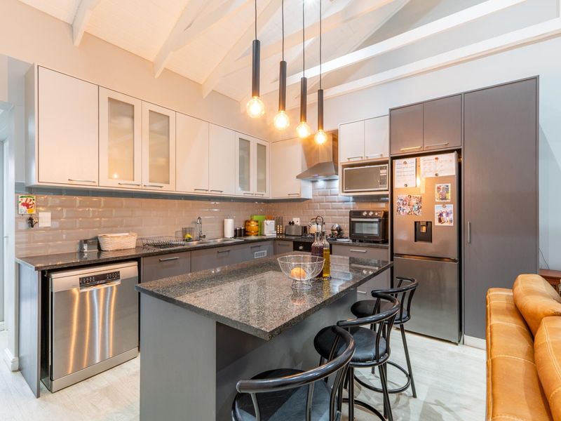 Modern kitchen featuring granite countertops, subway tile backsplash, built-in cabinetry, and a central island with pendant lighting under a vaulted ceiling with exposed beams.
