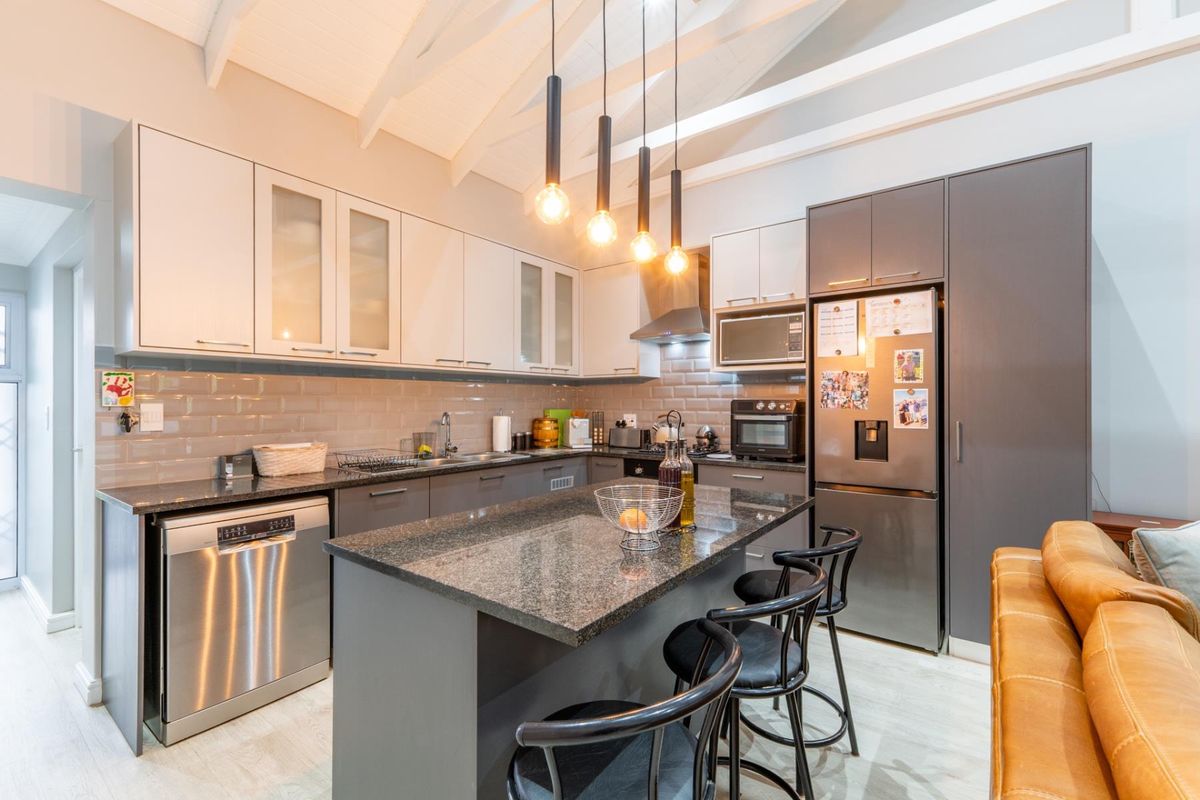 Modern kitchen featuring granite countertops, subway tile backsplash, built-in cabinetry, and a central island with pendant lighting under a vaulted ceiling with exposed beams.