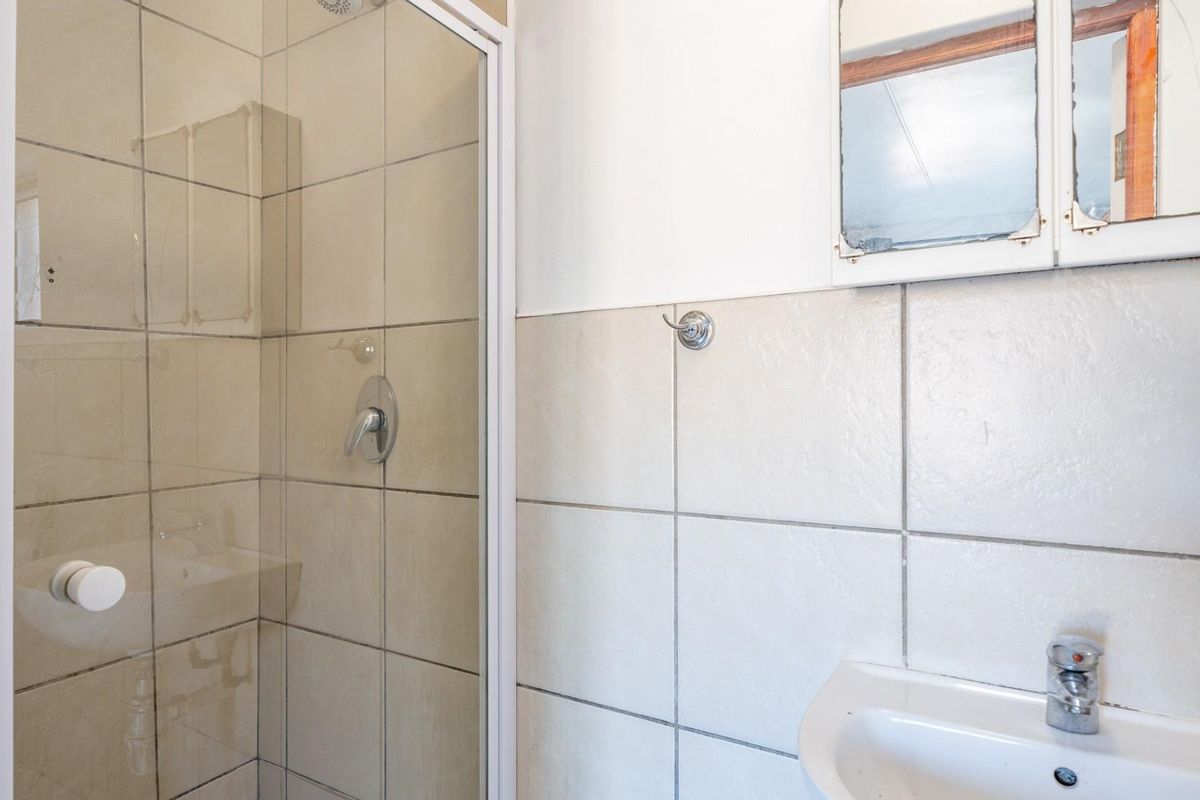 A functional bathroom featuring a shower enclosure with tiled walls, a pedestal basin, and a wall-mounted medicine cabinet.