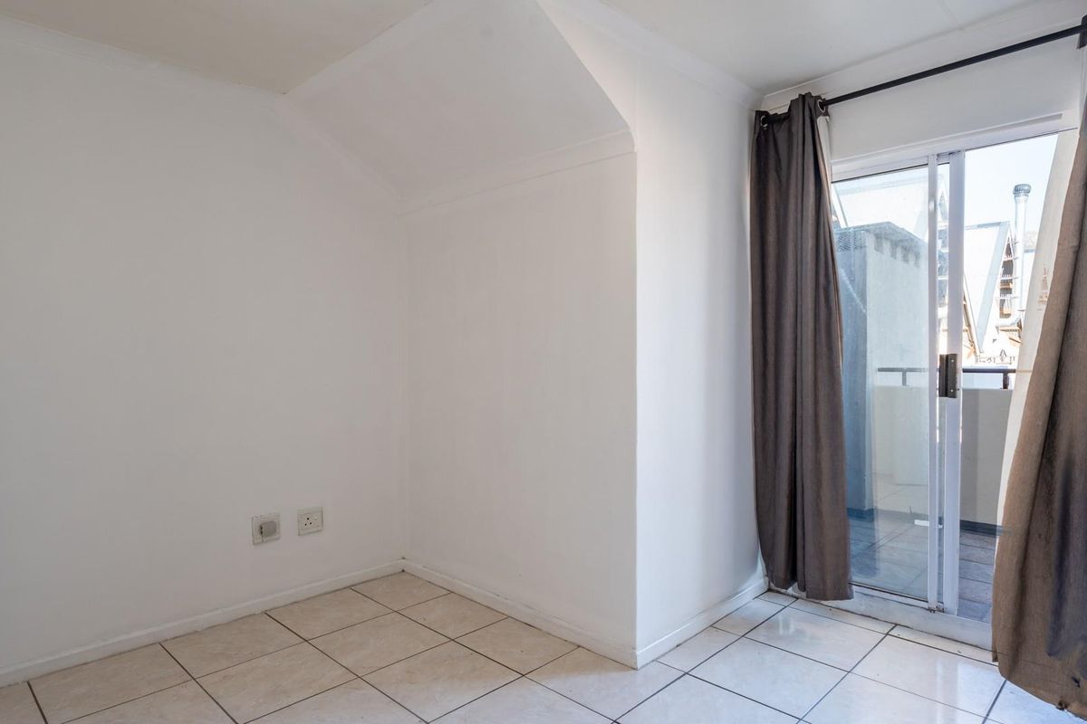 A bright, empty bedroom featuring tiled flooring, a sloped ceiling, and a sliding glass door providing access to an outdoor balcony.