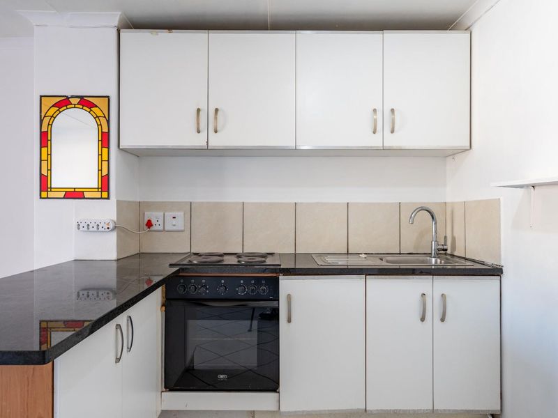 Compact kitchen featuring white cabinetry, granite countertops, a built-in oven with electric hob, and a stainless steel sink with tiled backsplash.