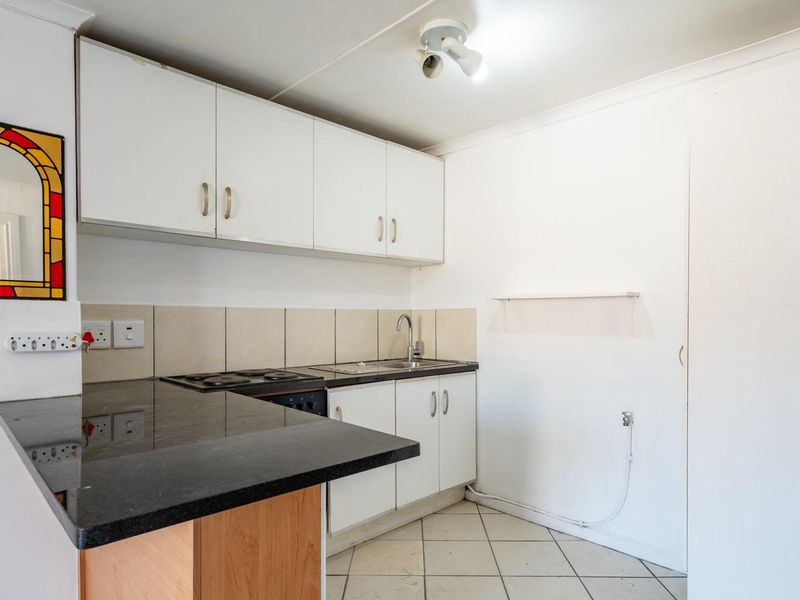 A compact kitchen featuring white cabinetry, a black granite countertop, an electric hob, and tiled flooring, offering a functional space ready for modernization.