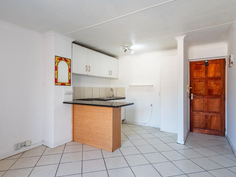A compact, empty kitchen area featuring built-in cabinetry, a laminate countertop with a sink, and tiled flooring, ready for a modern update.