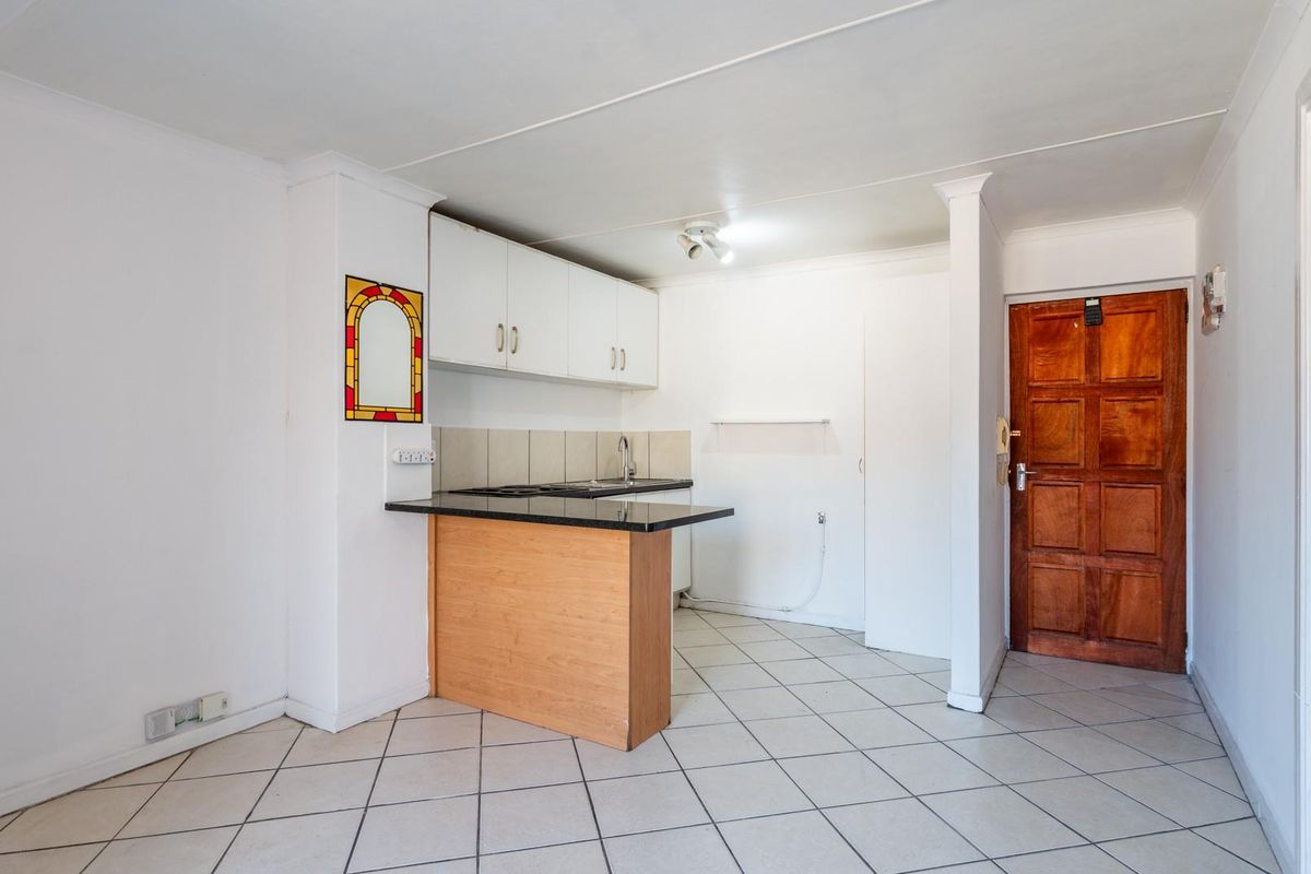 A compact, empty kitchen area featuring built-in cabinetry, a laminate countertop with a sink, and tiled flooring, ready for a modern update.